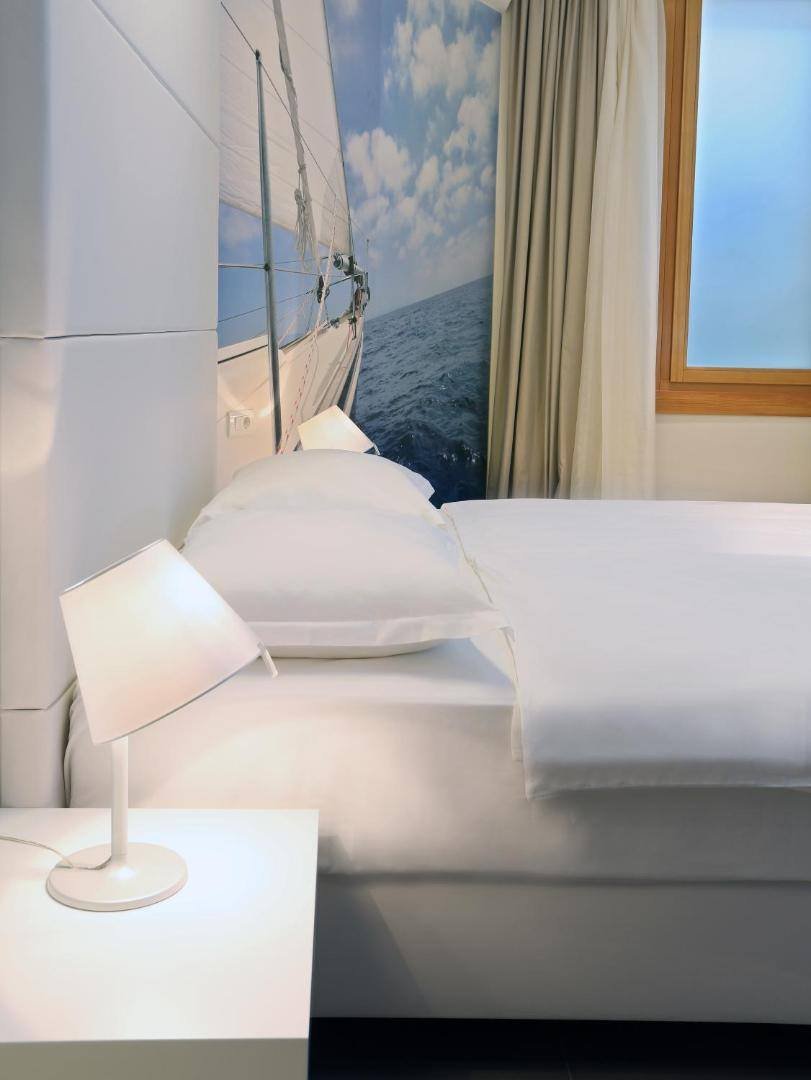 Double bed with white linen and a sailing mural by the window